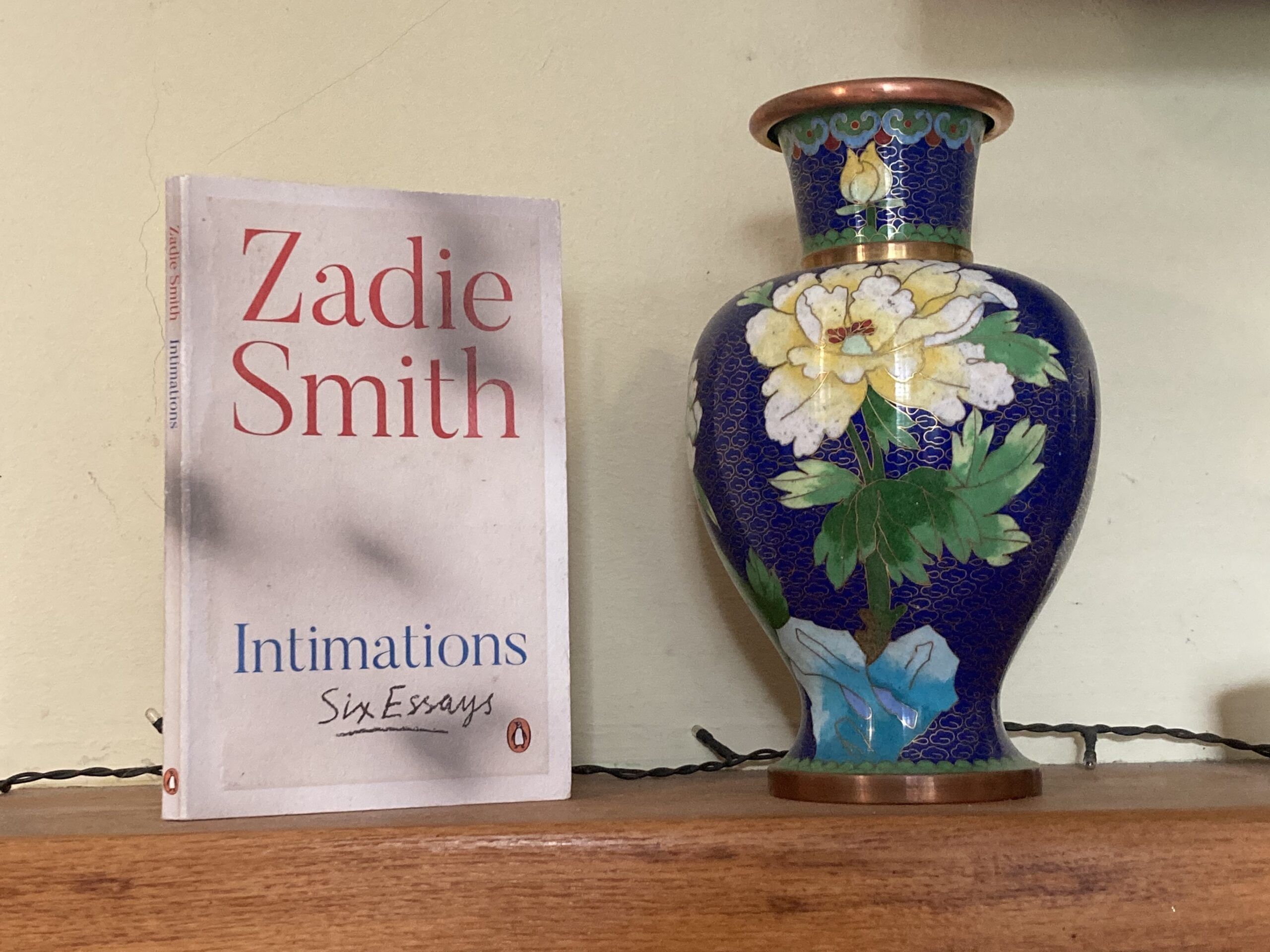 Intimations by Zadie Smith on a shelf next to a vase
