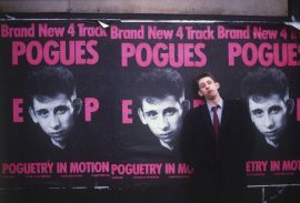 MacGowan stands before a commercial poster for punk band, The Pogues