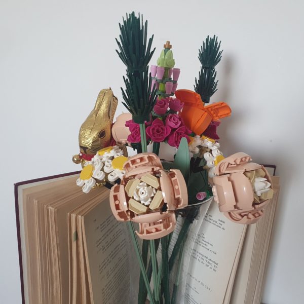 An opened grammar book with a transparent vase of Lego flowers in front of it and a slightly hidden chocolate bunny
