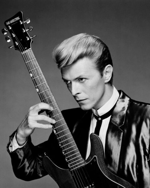 black and white david bowie holds a guitar