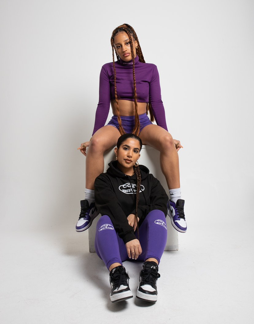 Two female models wearing the cozybrvnd's newest streetwear garments in purple and black