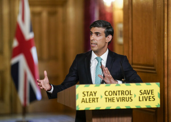 Rishi Sunak at a COVID-19 press conference. He stands behind a banner which reads "Stay Alert, Control the Virus, Save Lives".