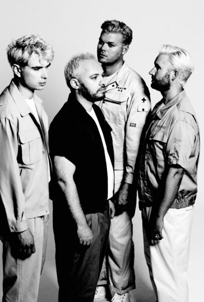 Monochrome photo of four men against a white background, all looking into the distance in different directions.