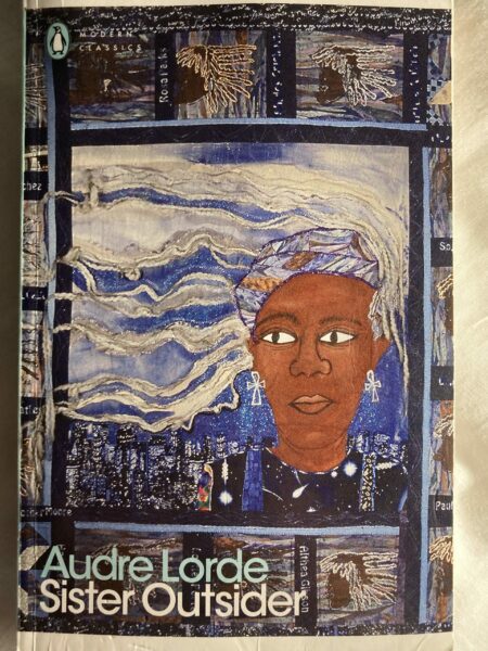 The front cover of Audre Lorde's essay collection 'Sister Outsider' featuring a black woman with her white hair flowing across the page against a background of a city. This is all highly stylised in a oil painting style.