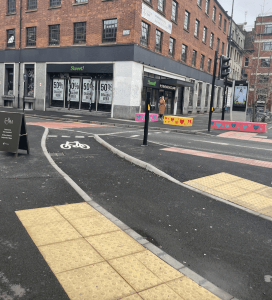 A pedestrian crossing at a cycle lane in Stevenson Square with no crossing lights, there are some drop curbs on either side of the cycle lane.