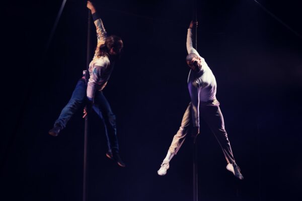 Two men hang onto a vertical pole each.