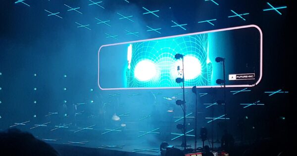 A concert stage with a giant projection of a blue futuristic looking face