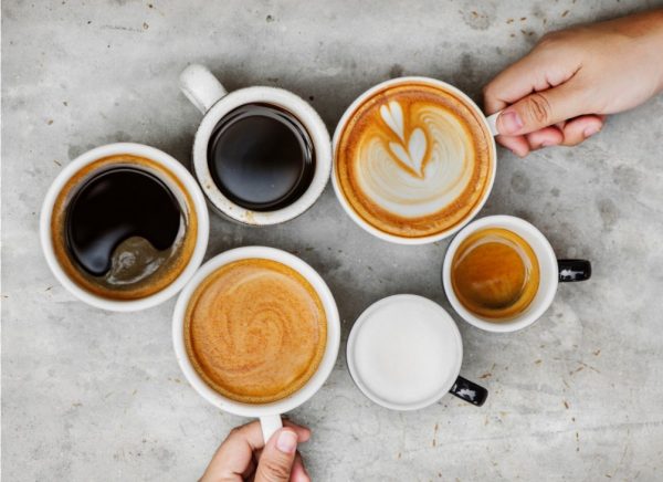 different types of coffee in six cups, with two hands holding two of the cups