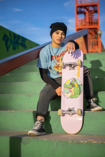 A skater wearing a beanie, graphic t-shirt and jeans, holding a skateboard