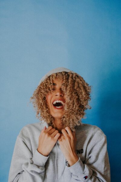 A woman with curly hair in a grey hoodie laughing