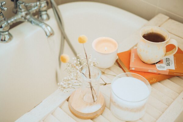 a white bath with a caddy holding a mug on top of books, a candle, and flowers