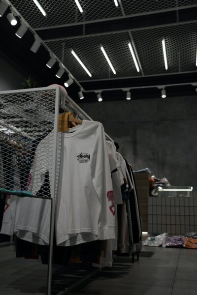 Photo shows a grey clothes store with a white Stüssy t-shirt hanging on a clothes rail at the front