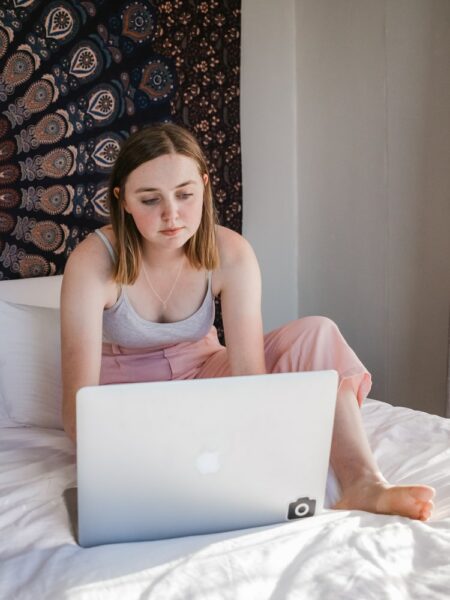 Woman sat on bed wearing loungewear on laptop